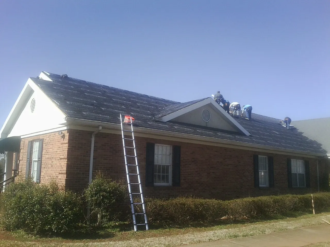 Crew tearing shingles off a brick ranch roof with a ladder set — Emergency Roof Repair work by our crew in Nicoma Park