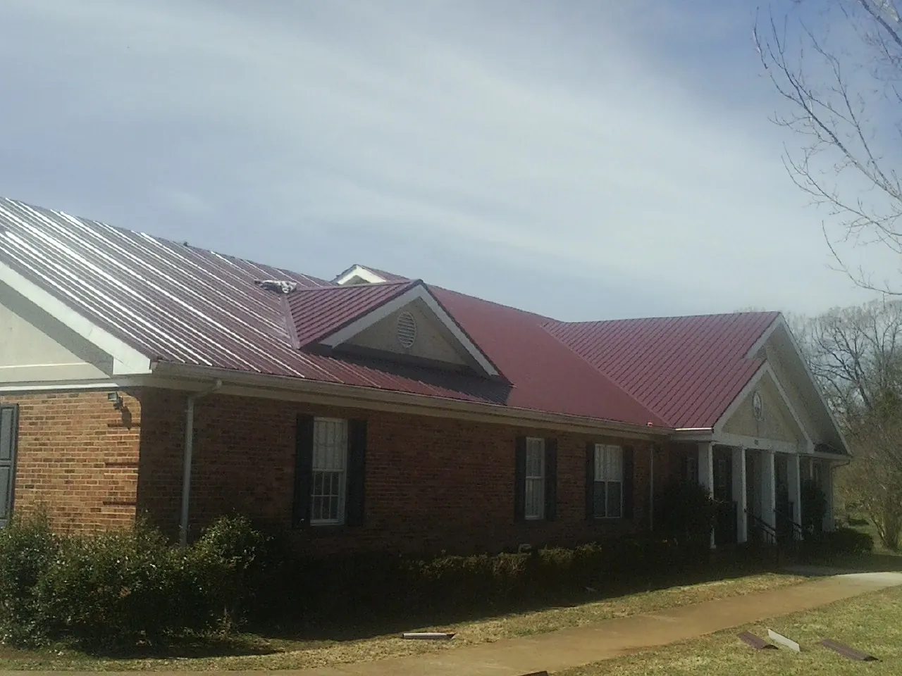 Red metal roof with gabled entries on a long brick building, from a Hail Damage Roof Repair job in Nicoma Park