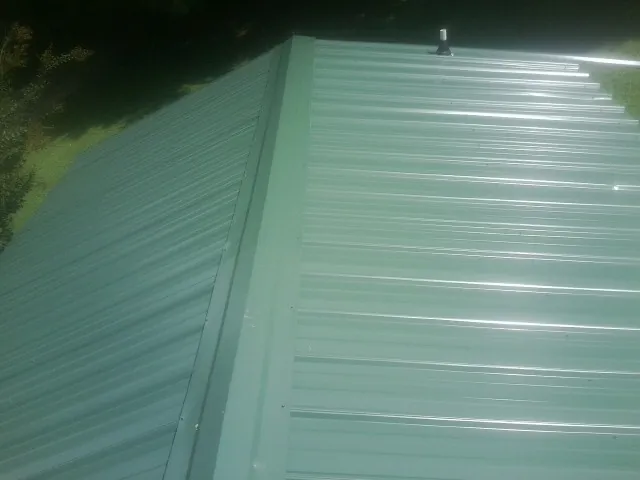 New green metal panels meeting at the ridge of a roof — Flat Roof Repair work by our crew in Nicoma Park