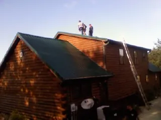 Crew on the ridge of a green metal roof on a two story log home in Nicoma Park