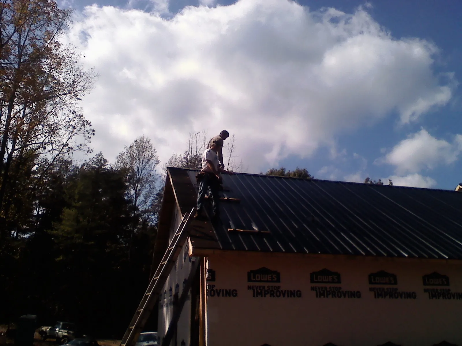 Roofer fastening dark metal panels high against a cloudy sky, from a Roof Inspection job in Nicoma Park