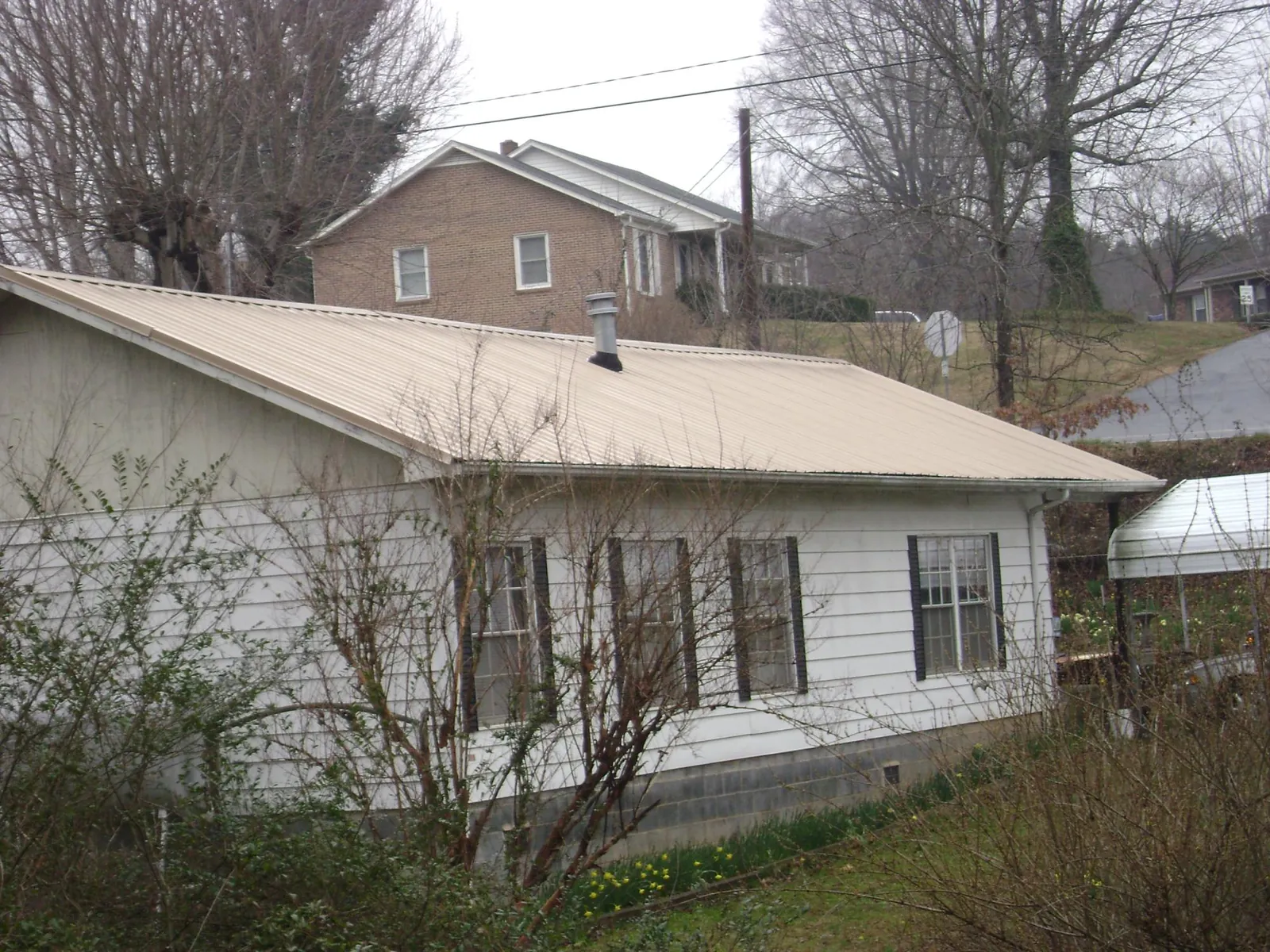 Tan metal roof on a white sided house set into a hillside — Commercial Roofing by Roofing Brothers in Nicoma Park